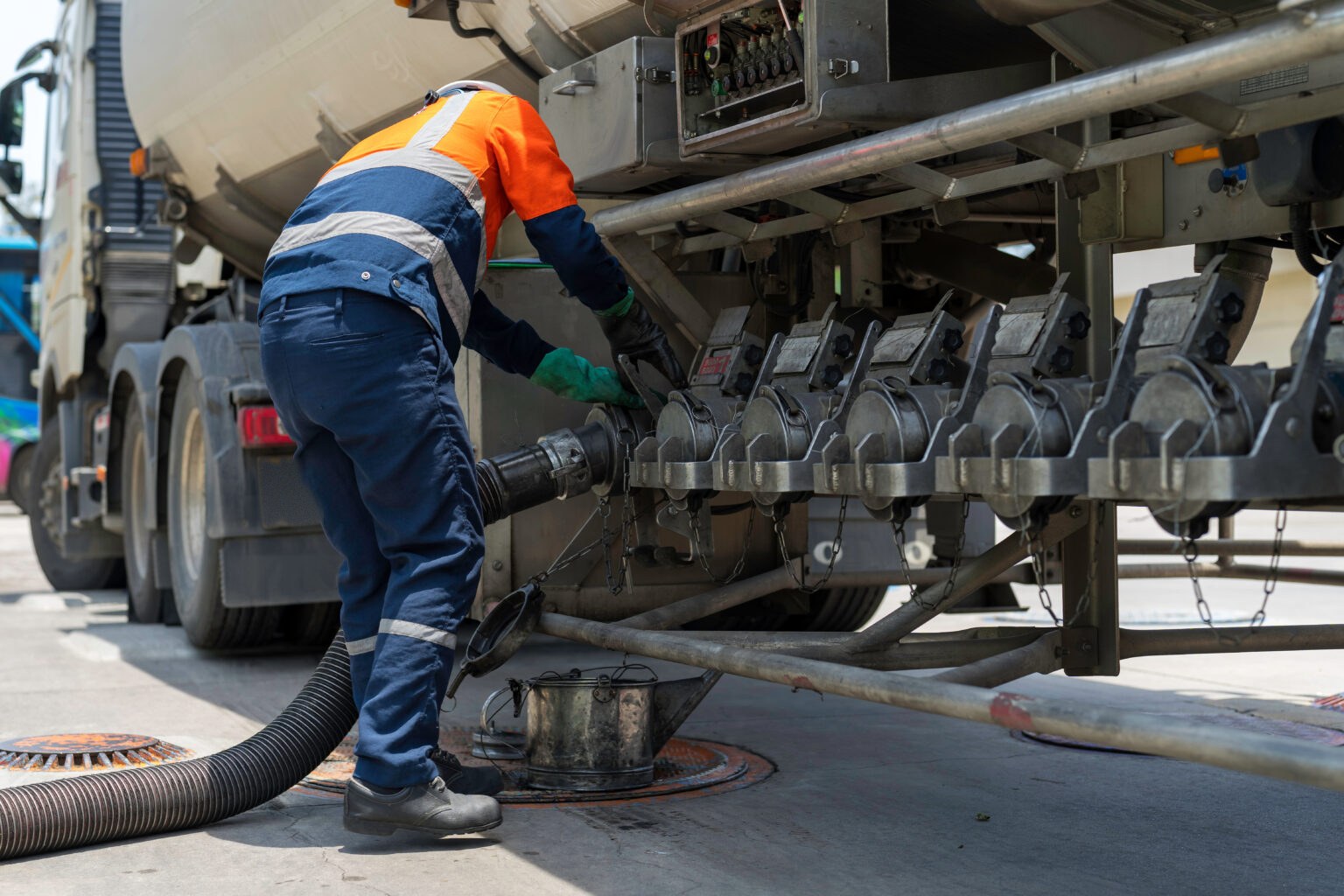 Fuel delivery driver connecting a hose to a tanker